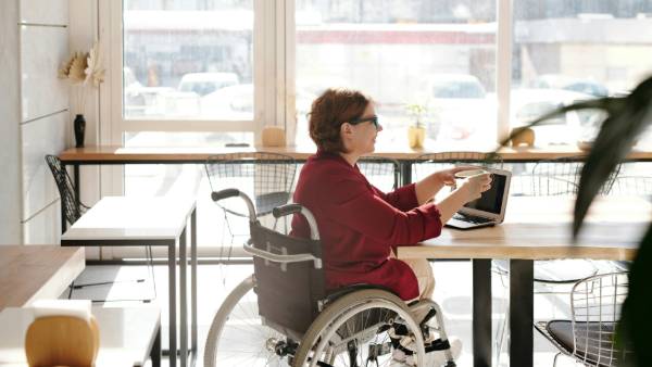 Woman in wheelchair enjoying access to a coffee shop working on laptop